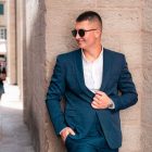 Confident man in a blue suit leans against a stone wall in charming Kotor, Montenegro.