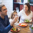 A happy family of four enjoying a meal with salads and wine at home.