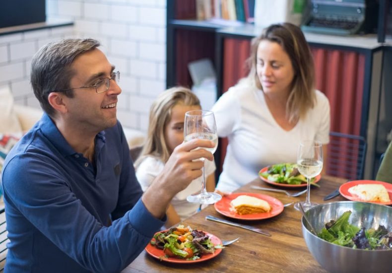 A happy family of four enjoying a meal with salads and wine at home.