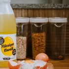 Liquid egg product bottle with cracked eggs and flour on kitchen counter.