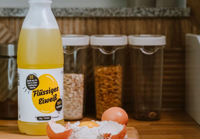 Liquid egg product bottle with cracked eggs and flour on kitchen counter.
