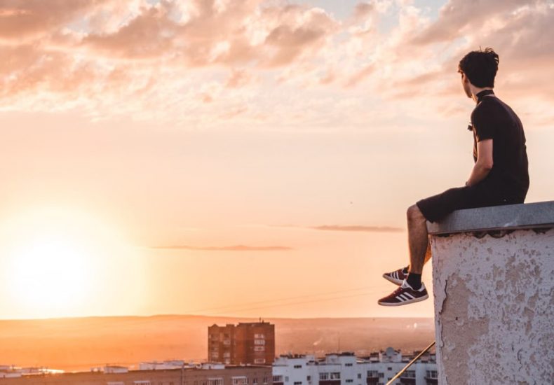 A young man sitting on a rooftop in Ufa, Russia, watching a vibrant sunset.